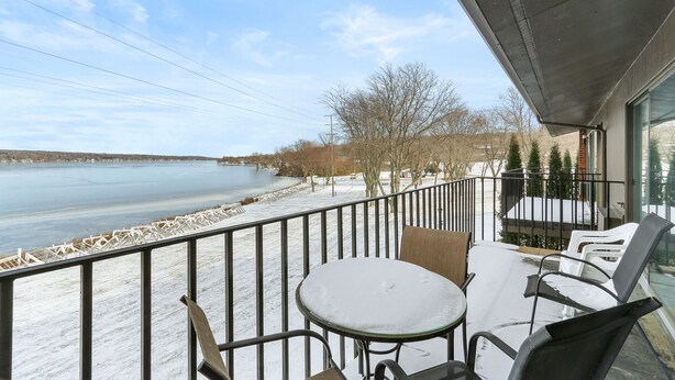 A balcony with a table and chairs, overlooking a body of water and a snow-covered landscape.