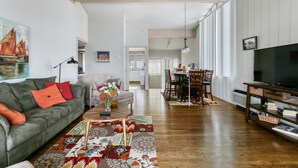 A spacious living room with a grey sofa, a coffee table, and a TV on a wooden stand.