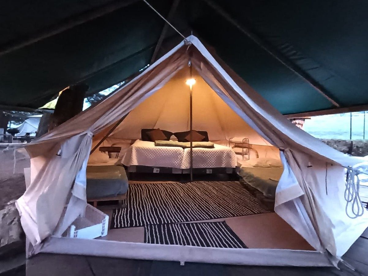 A tent with a bed and a small table, a light source, and a patterned mat on the floor.