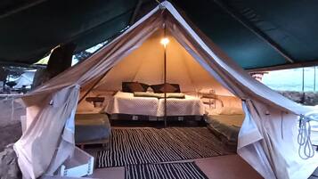 A tent with a bed and a small table, a light source, and a patterned mat on the floor.