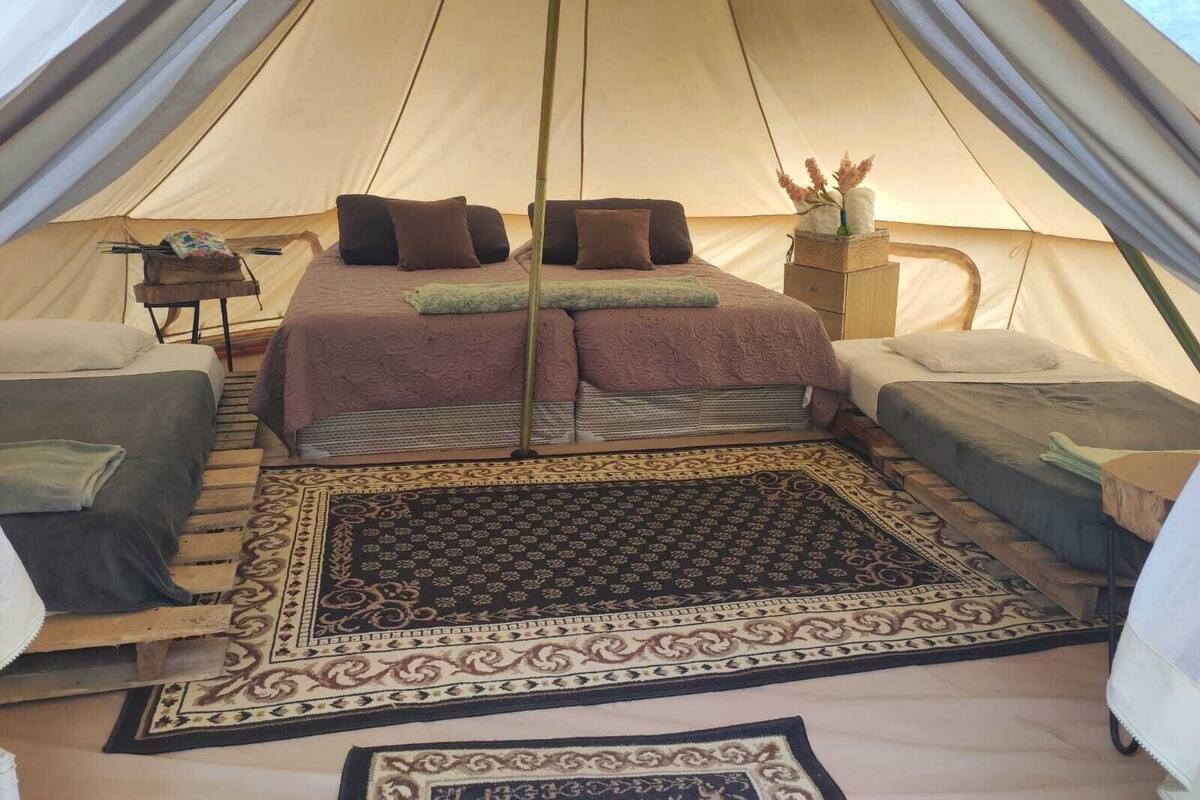 Une tente comprenant un lit, deux petits lits, un tapis et une petite table avec une lampe.