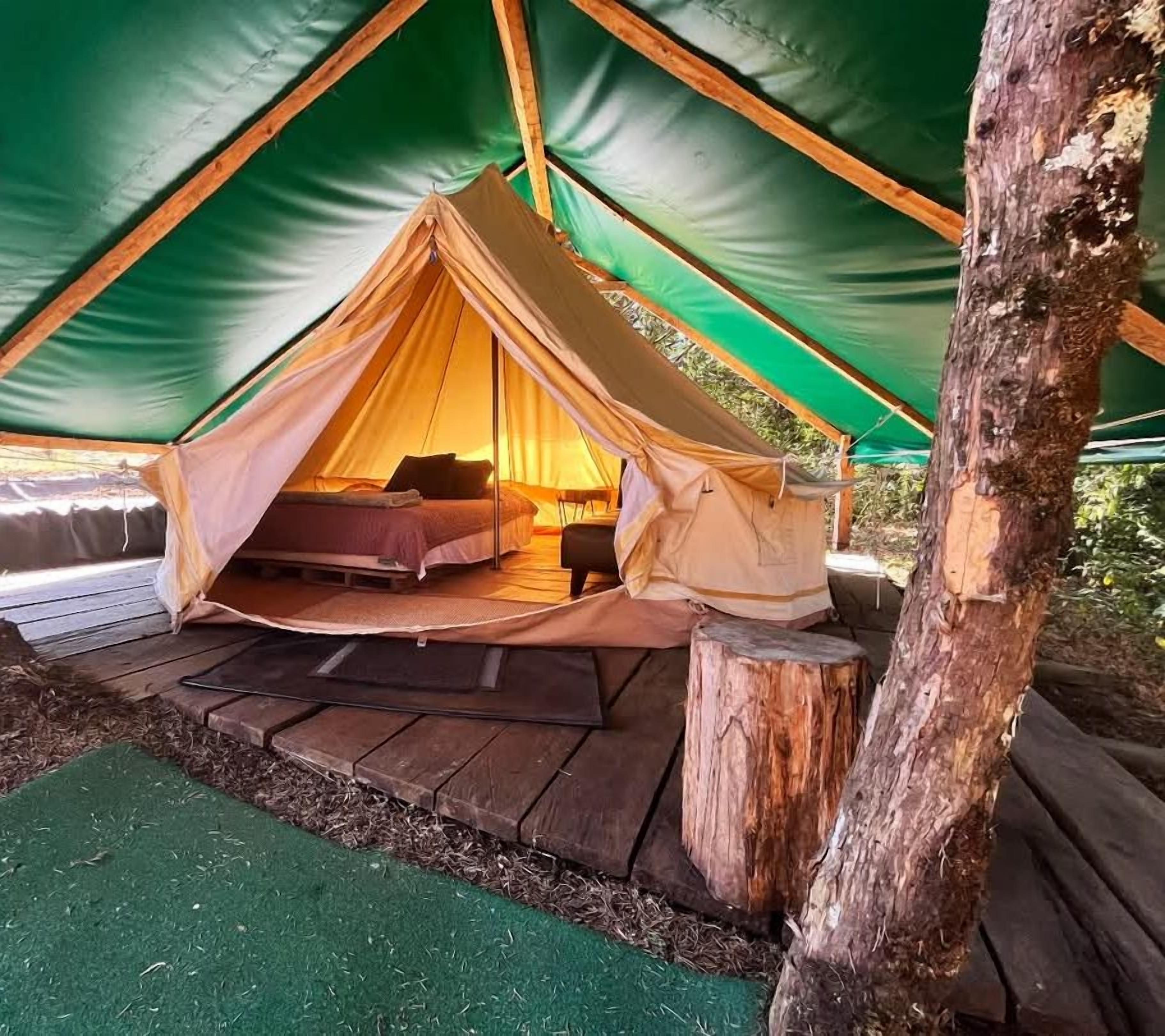 A tent with a bed inside, surrounded by a wooden deck and a green mat.