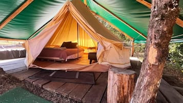 A tent with a bed inside, surrounded by a wooden deck and a green mat.
