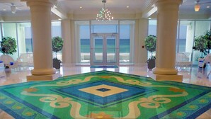Un vestíbulo con una alfombra grande y ornamentada, amplias ventanas con vista al océano y un par de puertas dobles que dan al exterior.