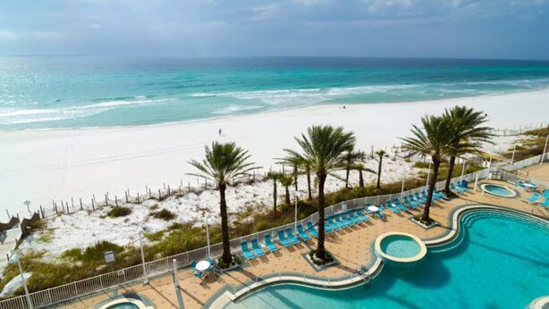 Un resort con piscina, acceso a la playa y palmeras.