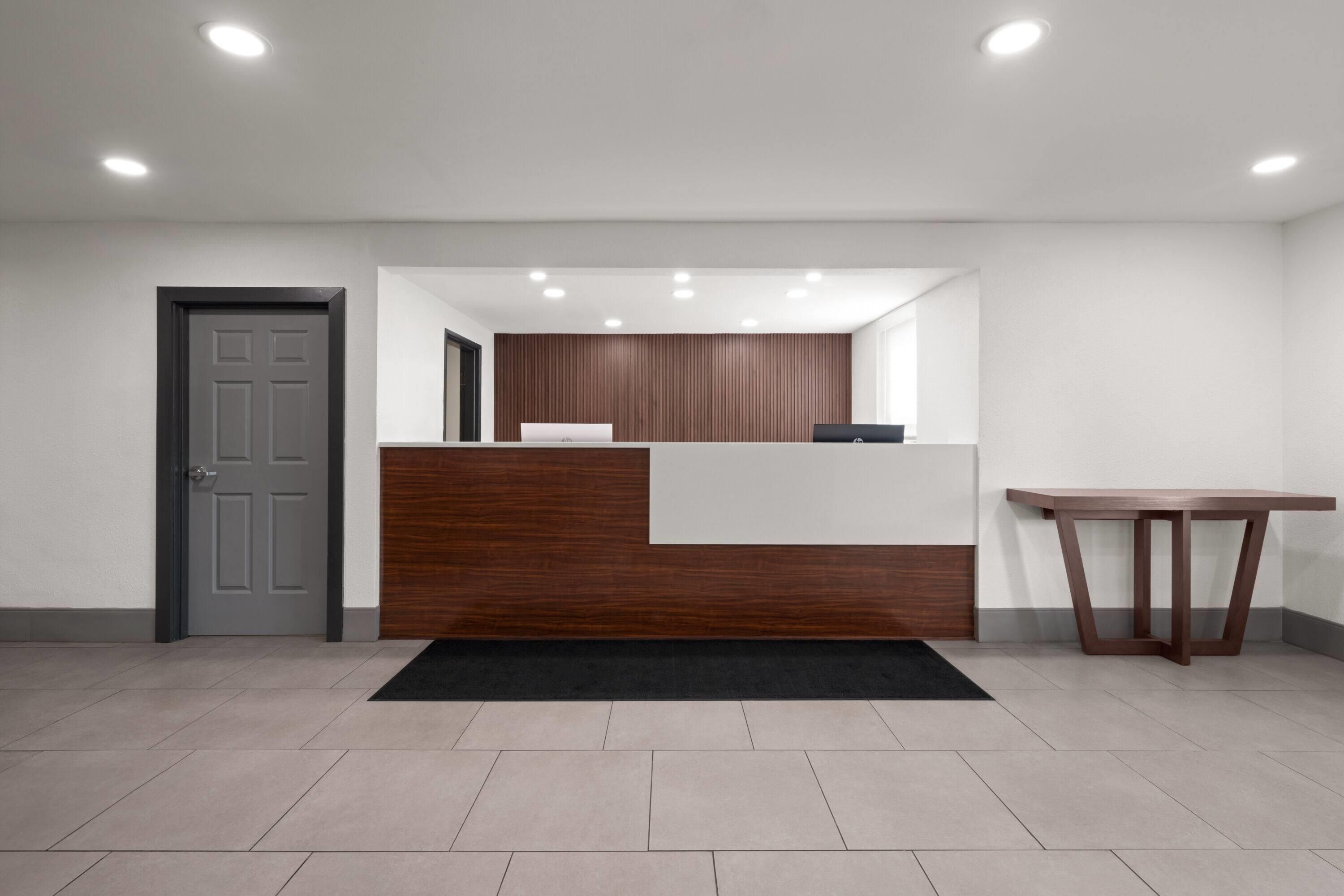 A reception area with a wooden reception desk, a black rug, a grey door, and a white wall.