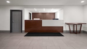 Una zona de recepción con un mostrador de madera, un tapete negro, una puerta gris y una pared blanca.