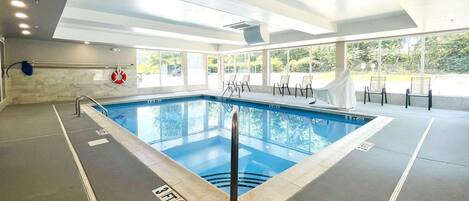 Une piscine intérieure à l’eau claire, équipée d’une bouée de sauvetage et d’un panneau indiquant une profondeur minimale de 90 cm (3 pieds) pour éviter de plonger.