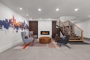 Una sala de estar moderna con chimenea, asientos cómodos, un mural con vista a la ciudad y una escalera.