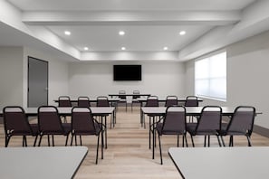 Un salón de conferencias con mesas, sillas, un televisor de pantalla plana y un ventanal grande.