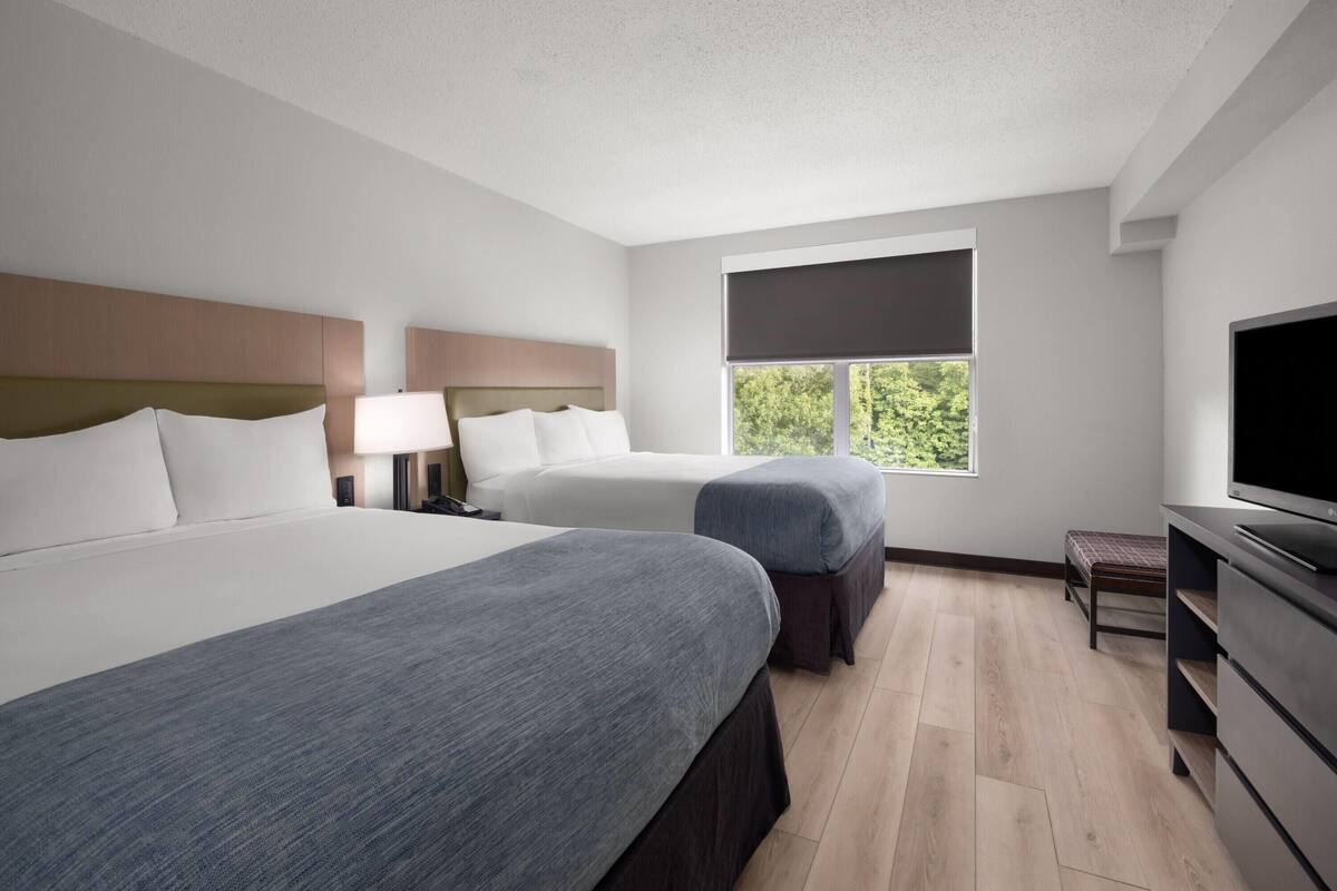 A hotel room with two beds, a television, a window with a view, and a desk.