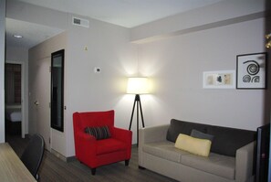 Una habitación con un sillón rojo, un sofá, una lámpara de pie y un televisor de pantalla plana.