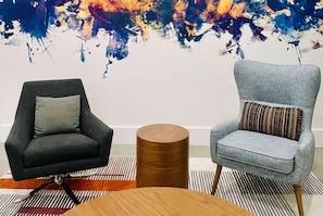 Dos sillones con cojines, una mesa redonda de madera y un cuadro abstracto grande en la pared.