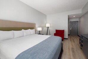 A hotel room with a large bed, two bedside lamps, a red chair, a desk, and a door.