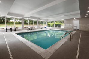 Ein moderner, überdachter Schwimmbereich mit Glaswänden, Fliesenboden und einer Metallleiter.
