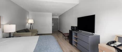 Habitación de hotel con cama, escritorio, televisor, lámpara, sofá y puerta que da a otra habitación.