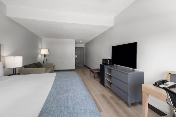 Habitación de hotel con cama, escritorio, televisor, lámpara, sofá y puerta que da a otra habitación.