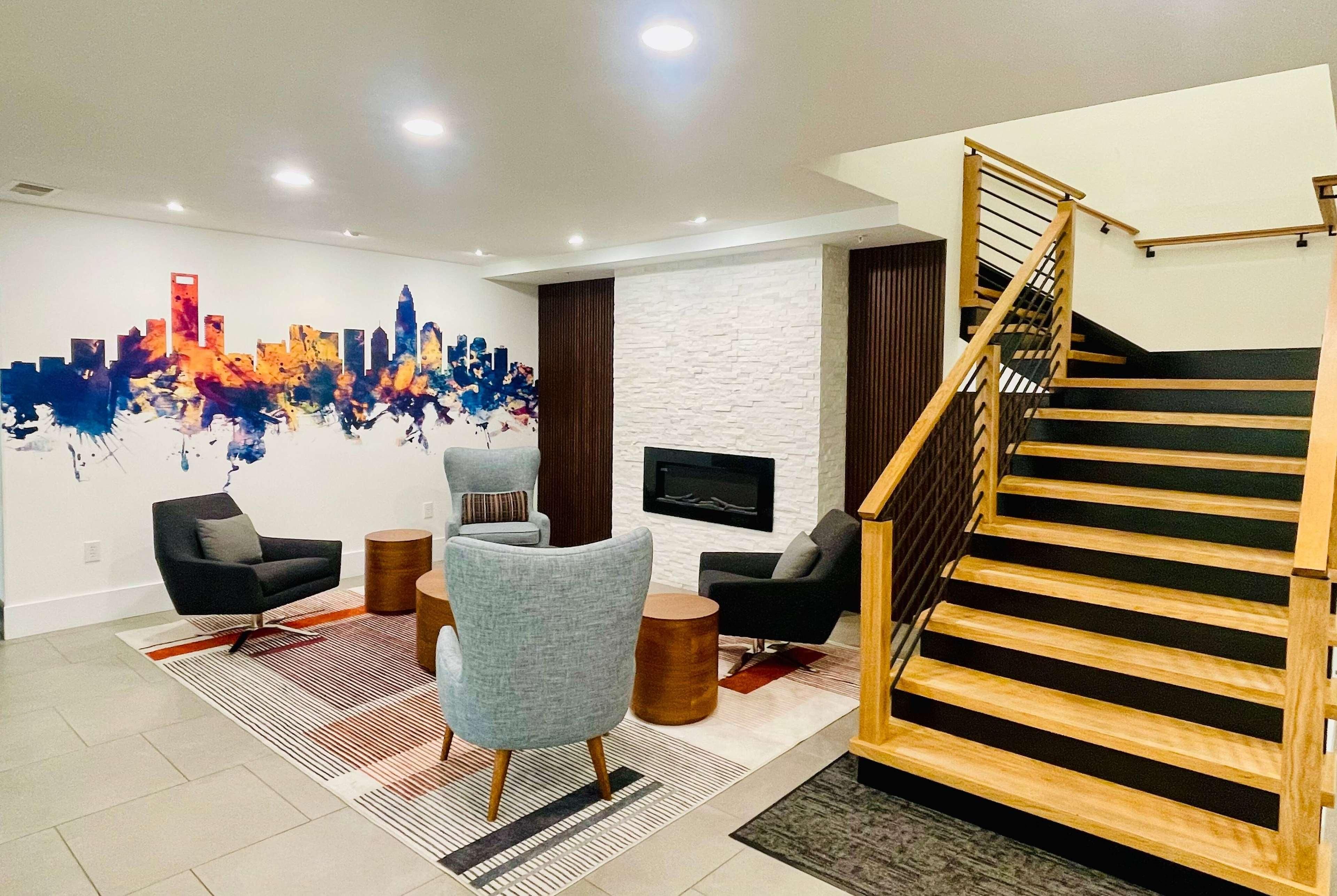 Una sala de estar moderna con un mural de un paisaje urbano, una escalera y un televisor de pantalla plana montado en la pared.