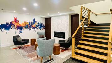 A modern living room with a cityscape mural, a staircase, and a flat-screen TV mounted on the wall.