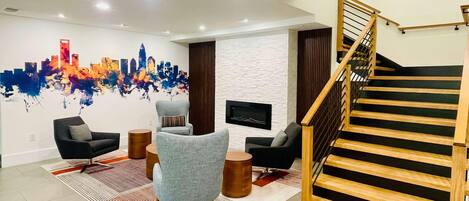 Una sala de estar moderna con un mural de un paisaje urbano, una escalera y un televisor de pantalla plana montado en la pared.