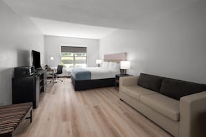 Una habitación de hotel moderna con una cama, un sofá, un escritorio con una computadora, un televisor y una ventana con vistas.