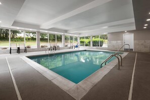 Una piscina interior moderna con paredes de vidrio transparente, suelo de baldosas y una escalera de metal.