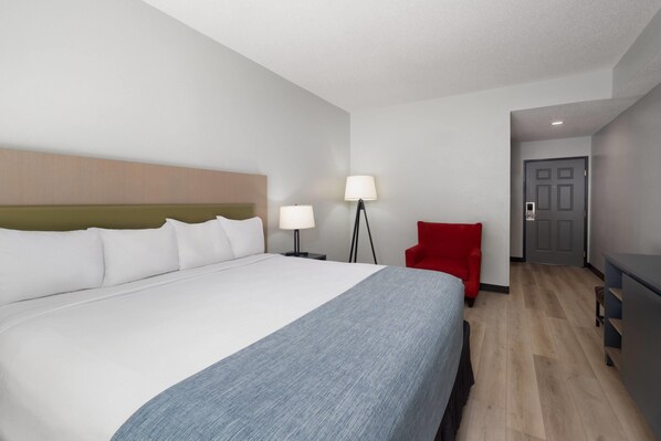 Ein Hotelzimmer mit einem großen Bett, zwei Nachttischlampen, einem roten Sessel, einem Schreibtisch und einer Tür.