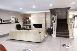 Una sala de estar moderna con un sofá, televisor y estanterías. Una escalera con barandilla conduce a otro nivel.