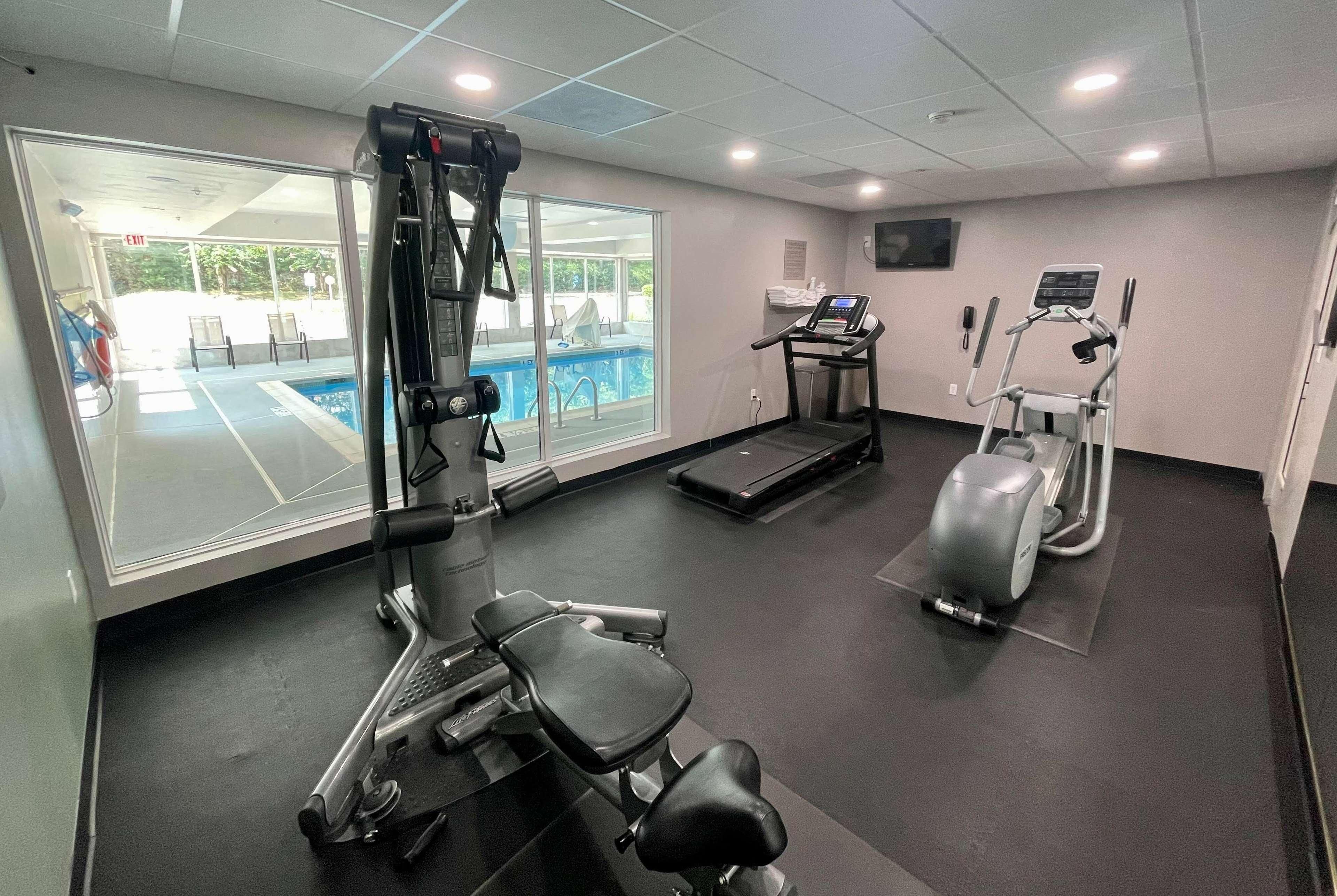 Un gimnasio con equipo de ejercicio, una cinta de correr y vistas a una piscina exterior.