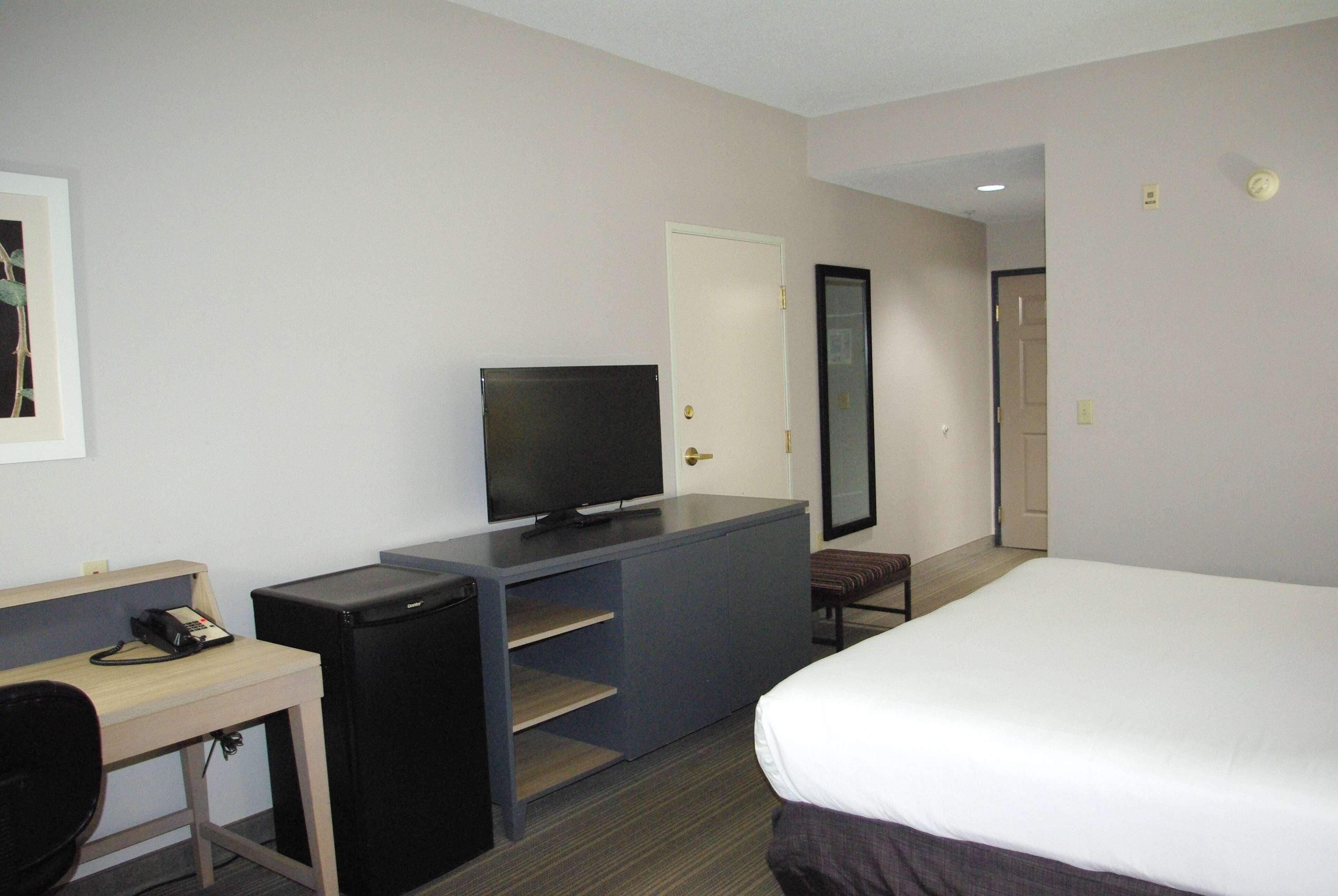 Una habitación de hotel con cama, escritorio con computadora, televisión y un pequeño espacio para sentarse.