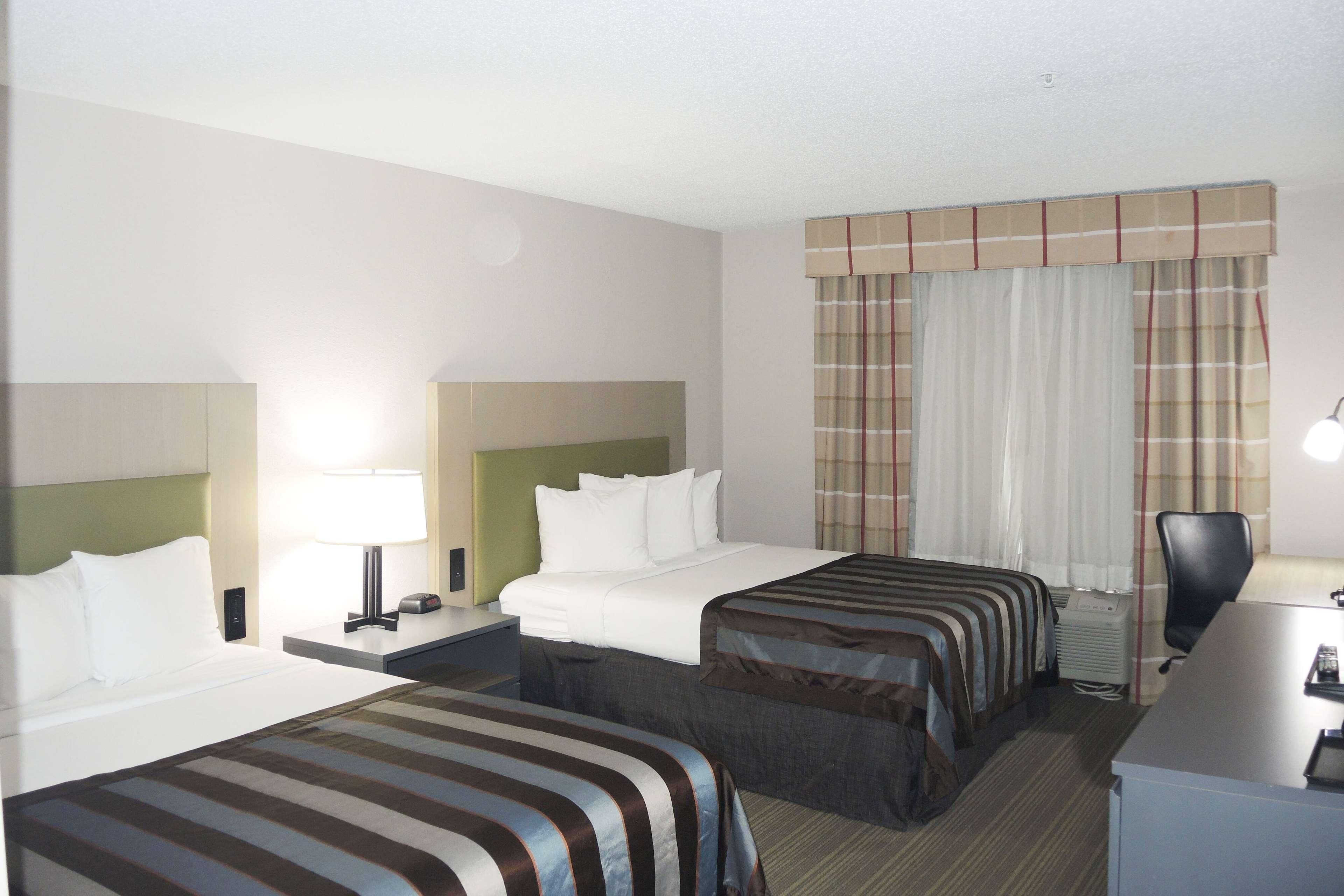 A hotel room with two beds, a desk, a chair, and a window with curtains.