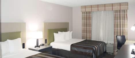 A hotel room with two beds, a desk, a chair, and a window with curtains.