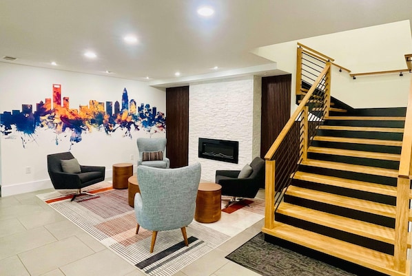 Una sala de estar moderna con un mural de un paisaje urbano, una escalera y un televisor de pantalla plana montado en la pared.