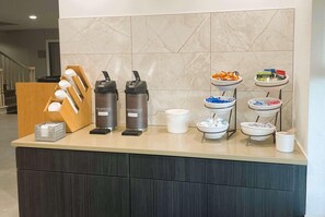 A hotel reception area with a marble wall, a wooden counter, and a buffet with various food items and condiments.