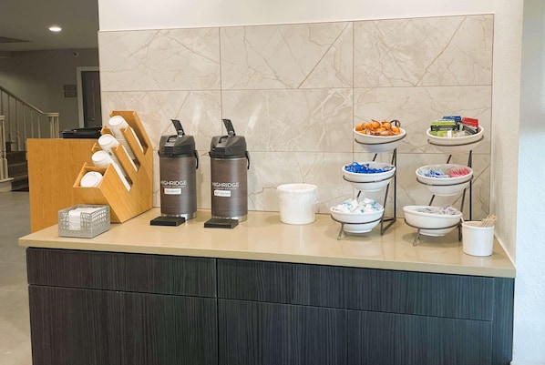A hotel reception area with a marble wall, a wooden counter, and a buffet with various food items and condiments.