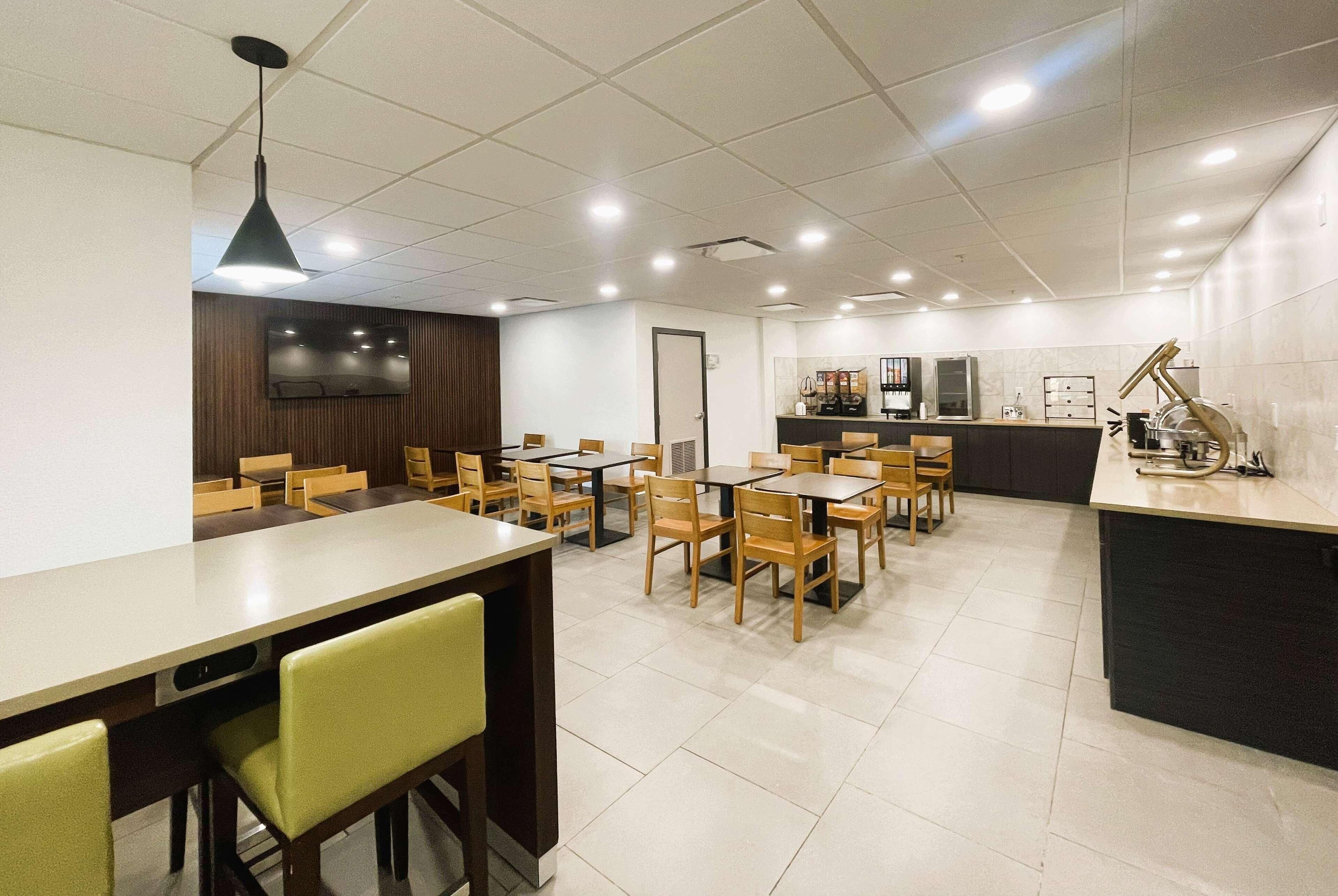 A modern dining area with multiple tables and chairs, a kitchen counter, and a television mounted on the wall.