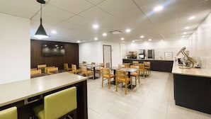 Un comedor moderno con varias mesas y sillas, una encimera de cocina y un televisor montado en la pared.
