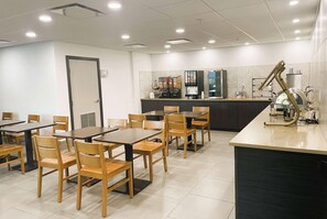 Un comedor con mesas y sillas, una encimera de cocina con electrodomésticos y una puerta.