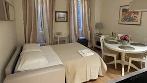 A hotel room with a bed, a dining table with chairs, a small table with a lamp, and a painting on the wall. - Cozy apartment-Florence old center-Duomo-Uffizi-2 bedrooms-2 bathrooms   (Firenze)