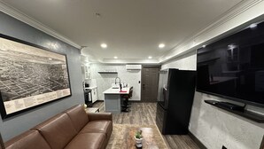 Una sala de estar moderna con un sofá de cuero marrón, una mesa de centro de madera con una planta y un televisor de pantalla plana grande montado en la pared.