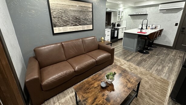 Una sala de estar moderna con un sofá de cuero marrón, una mesa de centro de madera y un cuadro con una vista de la ciudad.