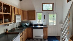 A compact kitchen with wooden cabinets, a microwave, a toaster, and a gas stove. - Webster Camp - rustic getaway with Webster Lake access, fire pit & large deck!   (Franklin)
