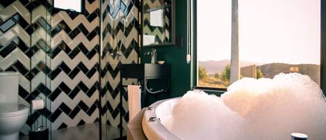 A modern bathroom with a large bathtub filled with bubbles, a mirror, and a view of the outdoors.
