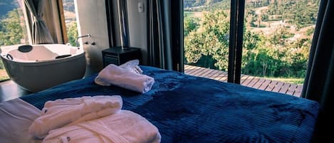 A bedroom with a large bed, a bathtub, and a view of the countryside.