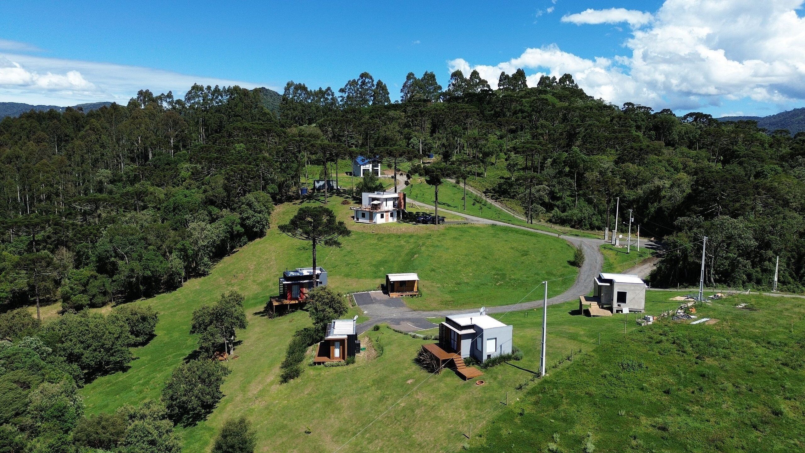 A remote, hilly area with several modern, single-story cabins surrounded by dense forest.