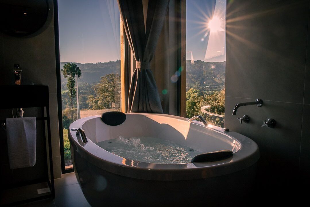 A bathroom with a large bathtub, a view of a mountainous landscape, and a window with curtains.