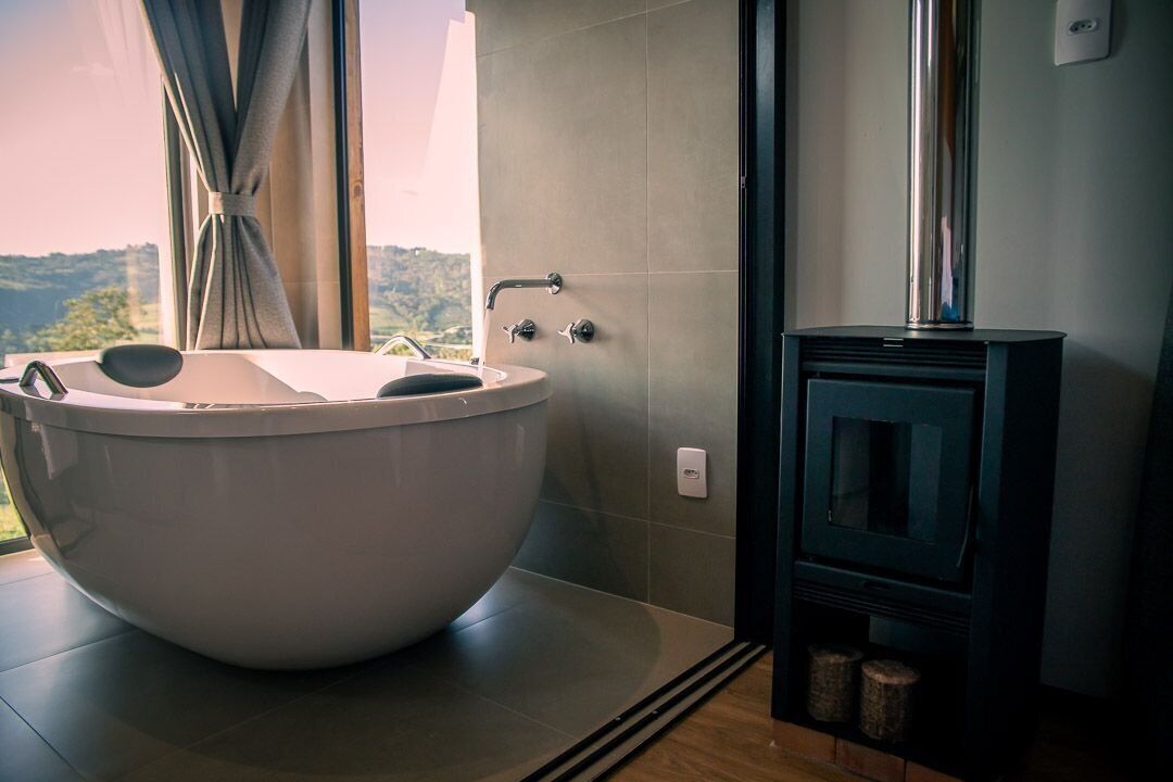 A modern bathroom with a large freestanding bathtub, a small sink, and a wood-burning stove.