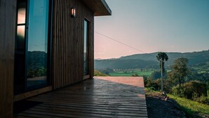 A modern building with large glass windows and a wooden deck overlooking a scenic landscape. - Cabanas Sunset View (Urubici)