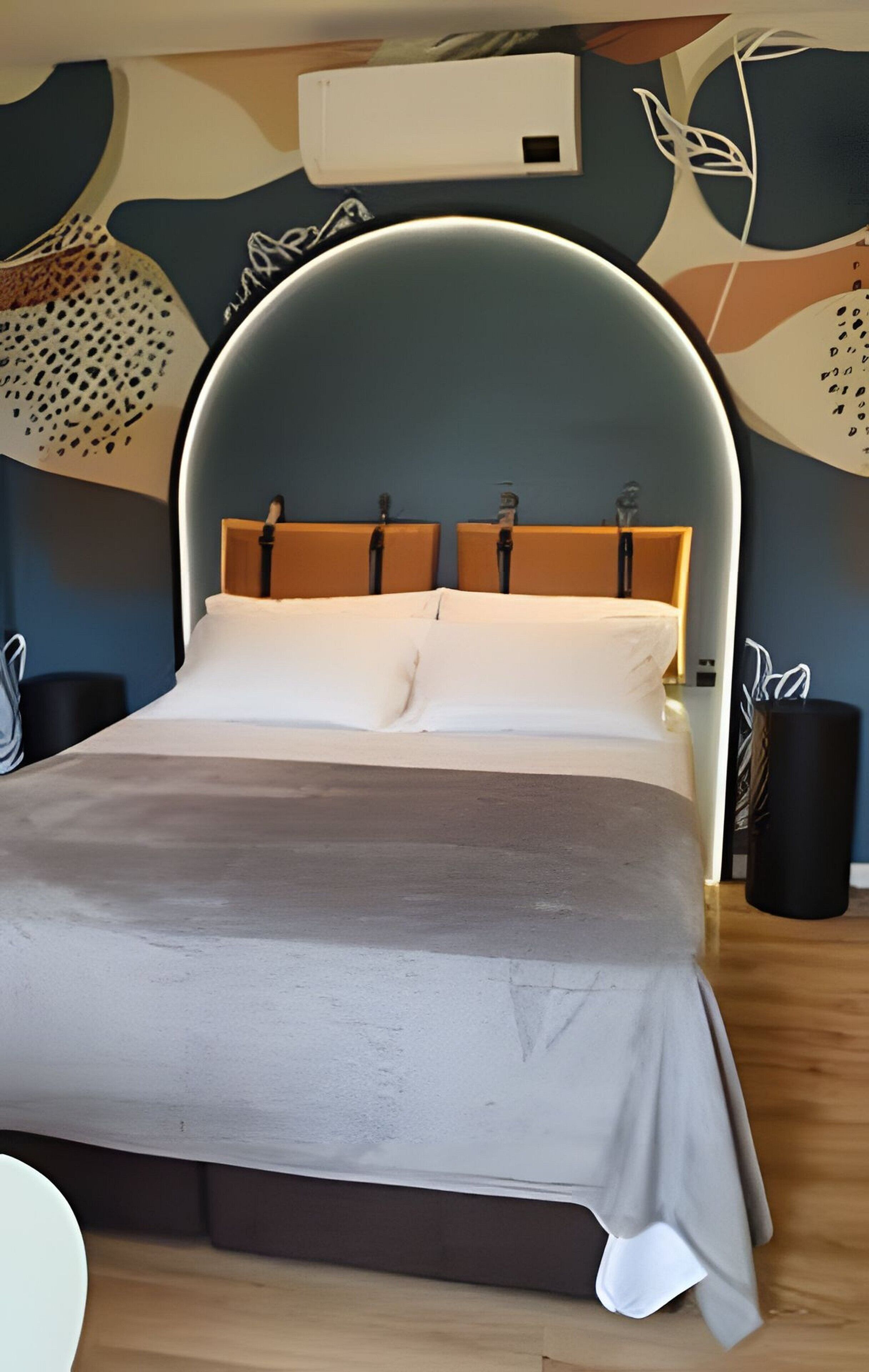 A modern bedroom with a curved bed, a wooden headboard, and a wall-mounted air conditioner.
