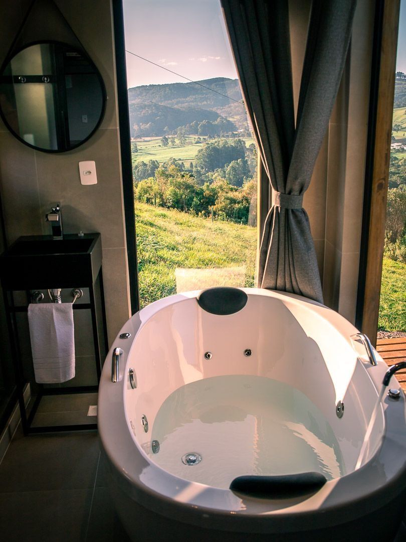 A bathroom with a large bathtub, a sink, a mirror, and a view of a green landscape through a window.